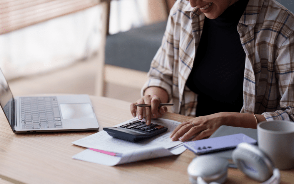 Vector art illustration of a person reviewing tax forms and documents on a desk, with a calculator and an open laptop nearby, symbolizing income tax preparation.